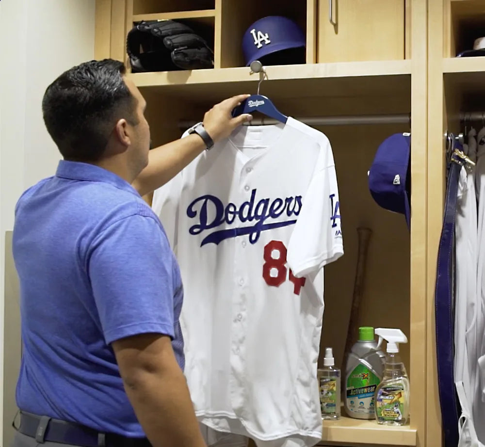 A Los Angeles Dodgers clubhouse attendant hanging a clean white home jersey in a locker stocked with Sweat X